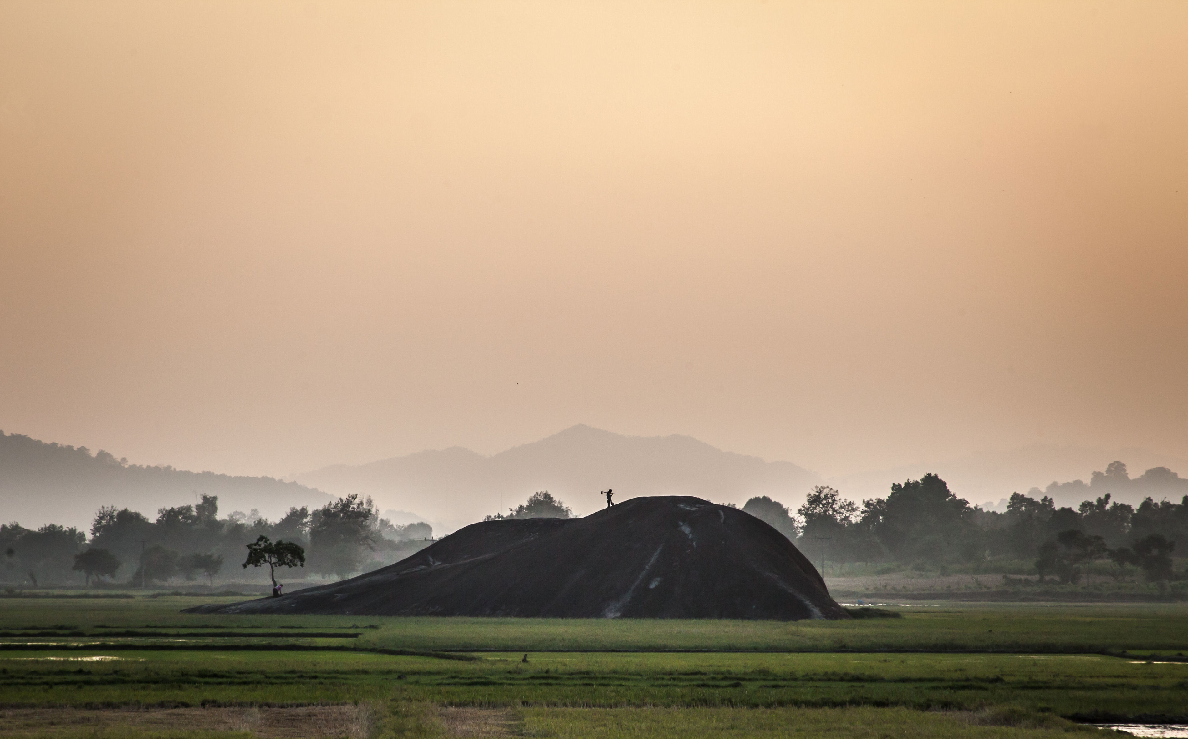 A worker silhouetted atop a large earthen mound in a rice field near Buôn Ma Thuột